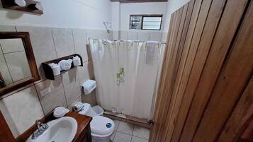Um banheiro pequeno com toucador de madeira, pia, vaso sanitário e cortina de chuveiro.