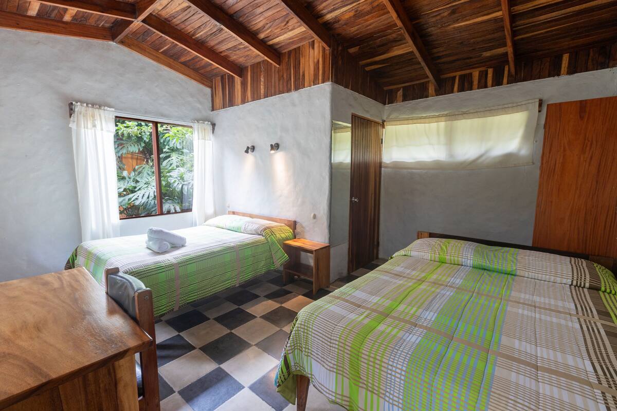A room with two beds, a wooden table, and a window with curtains.