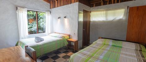 Una habitación con dos camas, una mesa de madera y un ventanal con cortinas.