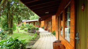 A covered walkway with wooden walls and a tiled floor, leading to a building with a green door marked '23'. - Elida Lodge Monteverde (Monteverde)
