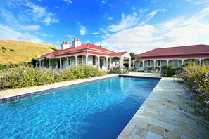 A swimming pool with a tiled edge, surrounded by a garden with flowering plants. - Cape South Estate - idyllic character property in rural setting close to beaches (Waimarama)
