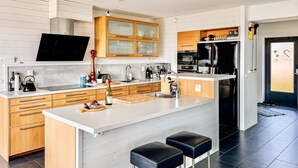 Uma cozinha moderna com armários de madeira, uma ilha grande com banquetas, forno embutido e geladeira.
