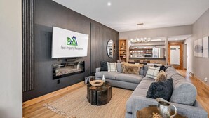 Una sala de estar moderna con un sofá gris, una mesa de centro y un televisor en la pared mostrando 'Peak Property Management'.