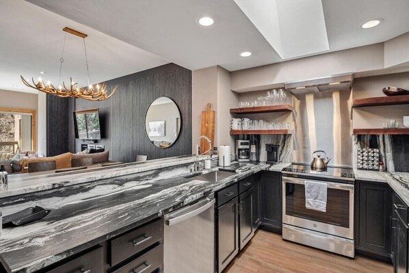 A modern kitchen with a marble countertop, stainless steel appliances, and a unique antler chandelier.