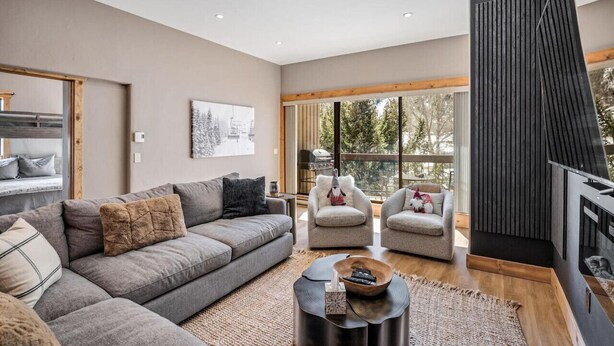 Una sala de estar moderna con un sofá seccional gris, dos sillones, una mesa de centro y una chimenea.
