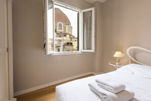 A hotel room with a bed, a window with a view of a building, a bedside table with a lamp, and a wall-mounted radiator. - Charming View apartment by Mmega (Firenze)