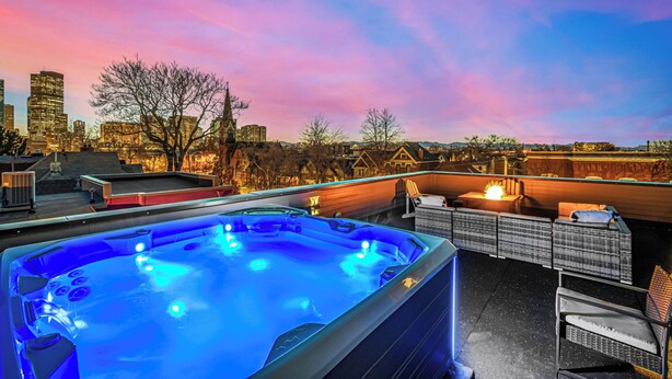 Una azotea con bañera de hidromasaje, mobiliario exterior y vistas a la ciudad al atardecer.