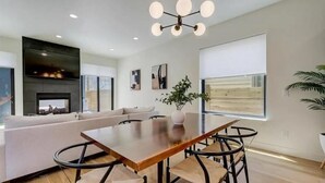 Una sala de estar moderna con una mesa de comedor de madera, sillas de metal negro, un sofá blanco y una chimenea.