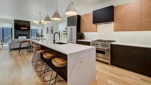 Una cocina moderna con una isla central, taburetes de bar, electrodomésticos de acero inoxidable e iluminación colgante.