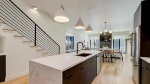 Cocina moderna con isla central, muebles negros y lámparas colgantes.