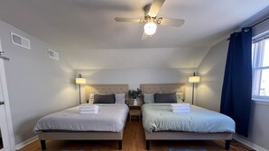 Ein Zweibettzimmer mit zwei Betten, Deckenventilator, Nachttischlampen und einem Fenster mit Vorhängen.