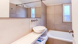 Un bagno moderno con una grande vasca, un lavandino bianco con lavabo, uno specchio e una finestra.