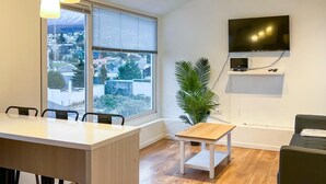 Un soggiorno moderno con una grande finestra, una TV a schermo piatto montata a parete, un tavolo da pranzo e un divano.