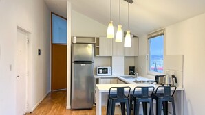 Una cucina moderna con frigorifero in acciaio inossidabile, forno a microonde e macchina da caffè. Due sgabelli da bar e una finestra con vista.
