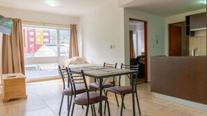 A dining area with a table and chairs, a small side table, and a view of buildings outside. - Mirador de los Cerros (Ushuaia)
