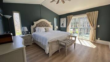 Quarto com uma cama grande, um ventilador de teto, uma mesa de cabeceira, uma luminária e uma janela com cortinas.