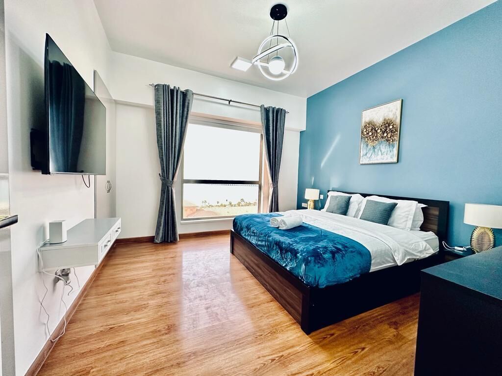 Een moderne slaapkamer met een bed, een bureau, een flatscreen televisie en een raam met gordijnen.