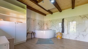 A bathroom with a marble wall, a bathtub, wooden flooring, and a ceiling with exposed beams.
