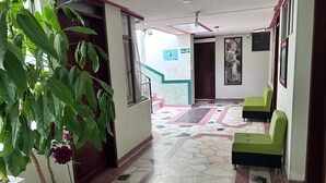 Un couloir avec une plante en pot, des sièges verts, un sol à motifs et un escalier.