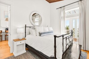 Quarto com cama, mesa de cabeceira, espelho e vista para o exterior.