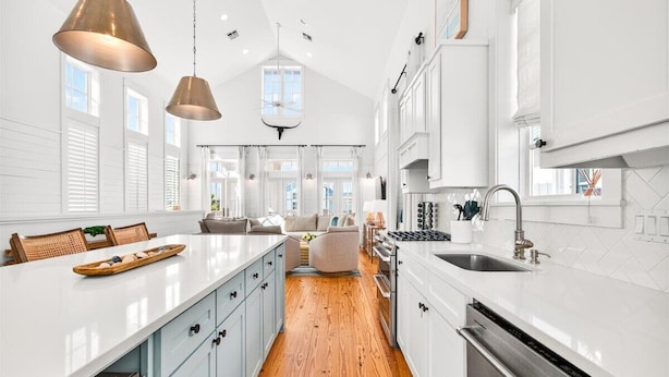 A modern kitchen with white cabinetry, a wooden floor, and pendant lighting. - Windsong 118 BE (Port Aransas)