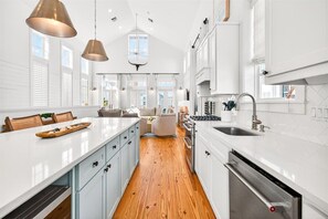 Uma cozinha moderna com armários brancos, piso de madeira e iluminação pendente.