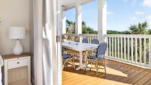 An outdoor patio with a table and chairs, a lamp, and a view of greenery. - Windsong 118 BE (Port Aransas)
