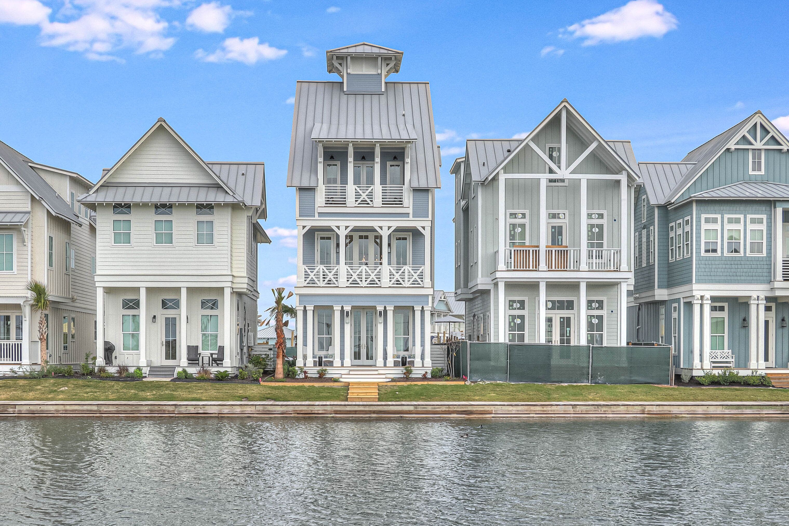 A row of waterfront houses with a central two-story house featuring a balcony and a small tower.