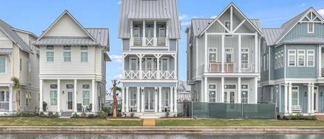 A row of waterfront houses with a central two-story house featuring a balcony and a small tower.