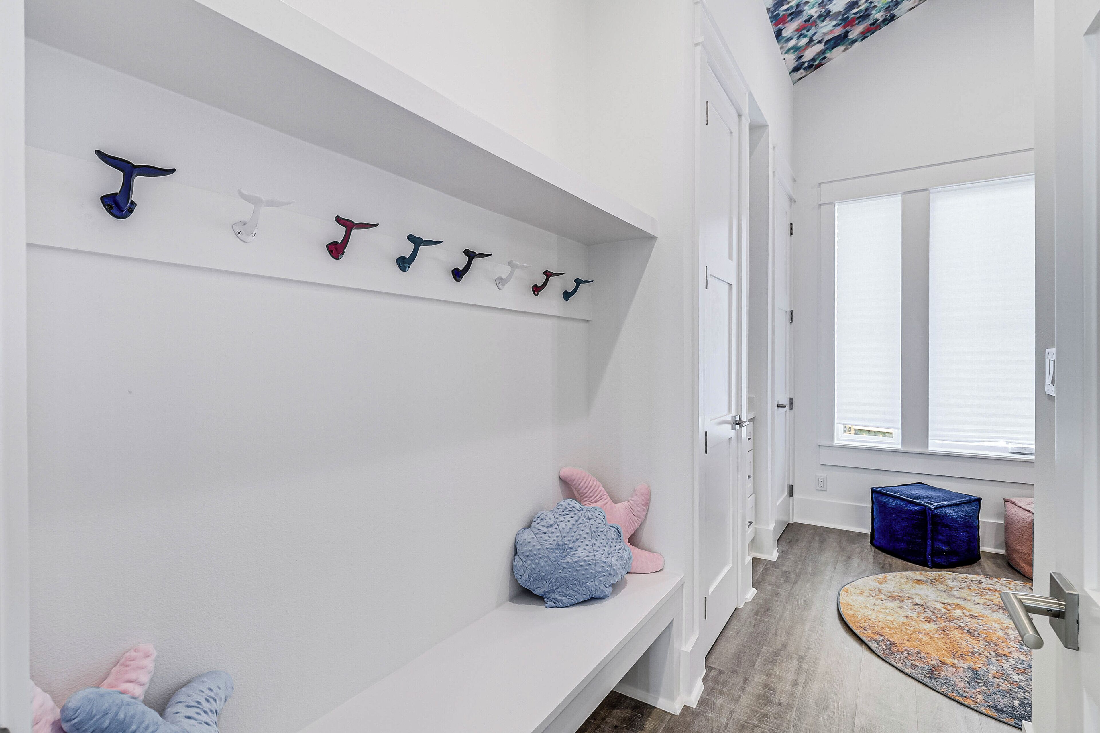 A hallway with a white wall, a bench, a rug, and a door with a window.