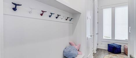 A hallway with a white wall, a bench, a rug, and a door with a window.
