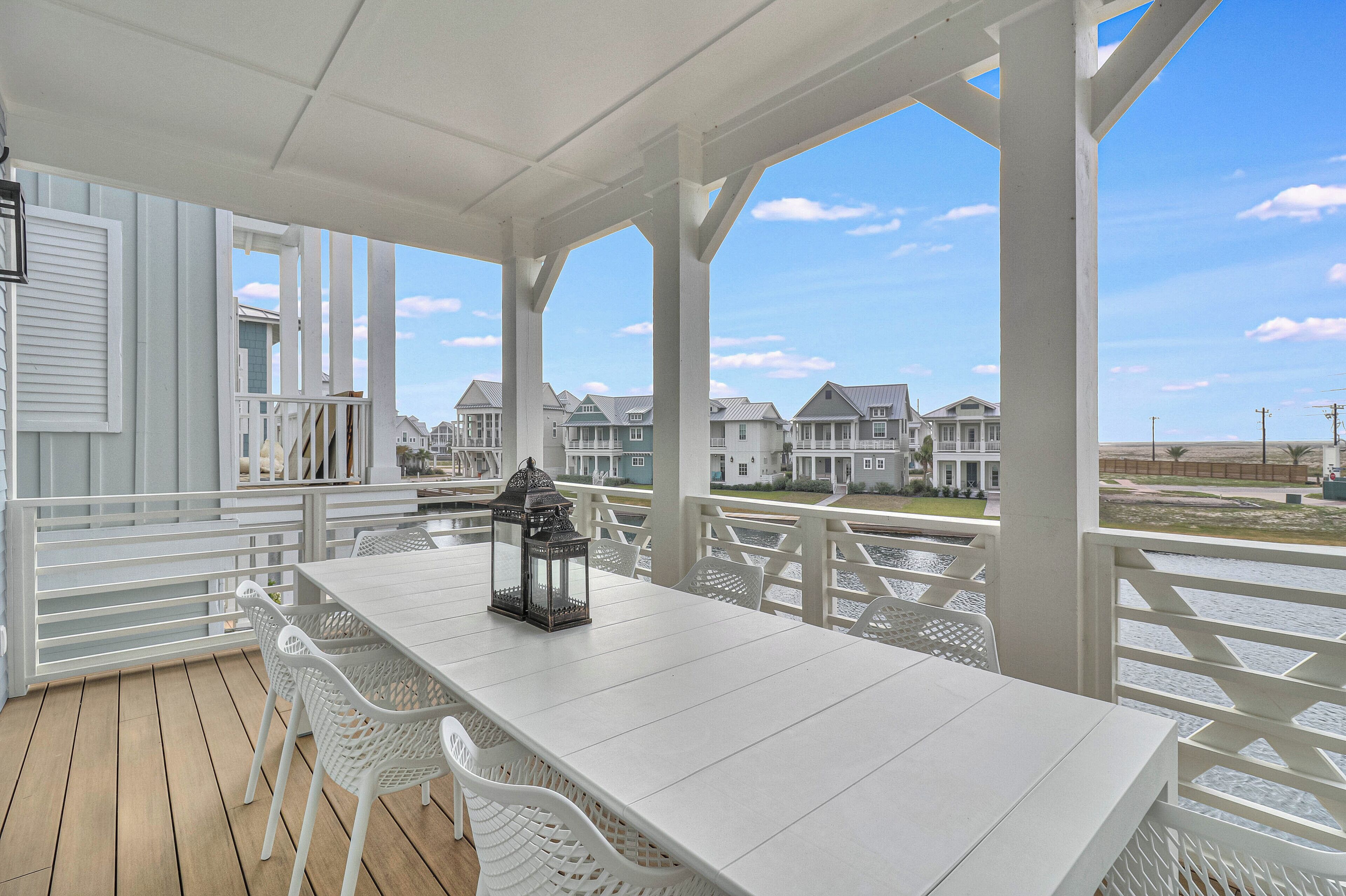 A covered outdoor area with a white table and chairs, a lantern, and a view of houses in the background.