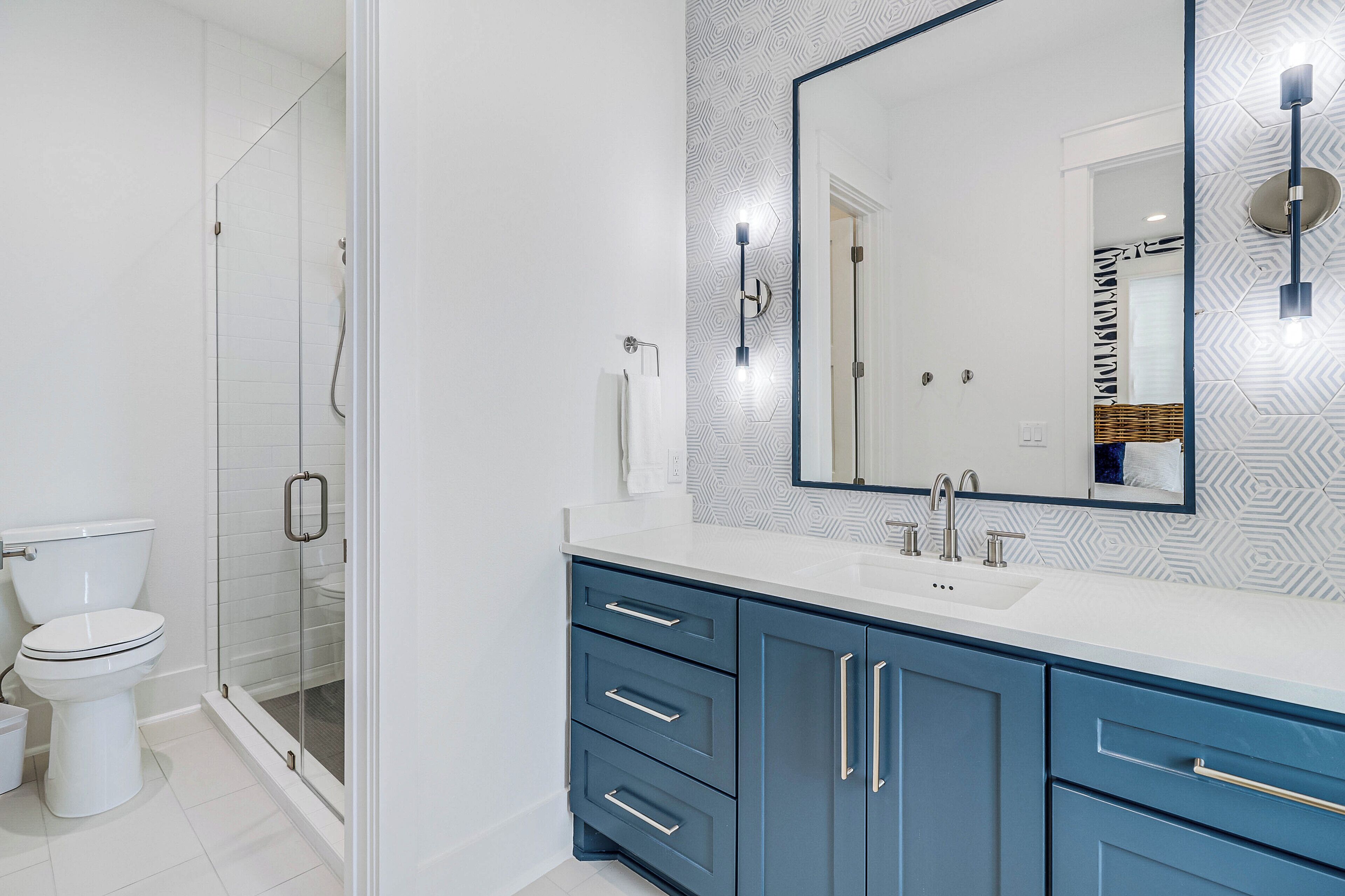 A modern bathroom with a glass shower enclosure, a white toilet, and a vanity with a large mirror and blue cabinets.