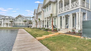 A row of coastal-style houses with a wooden boardwalk leading to a swimming pool. - Sea Vous Play 112 NEI (Port Aransas)