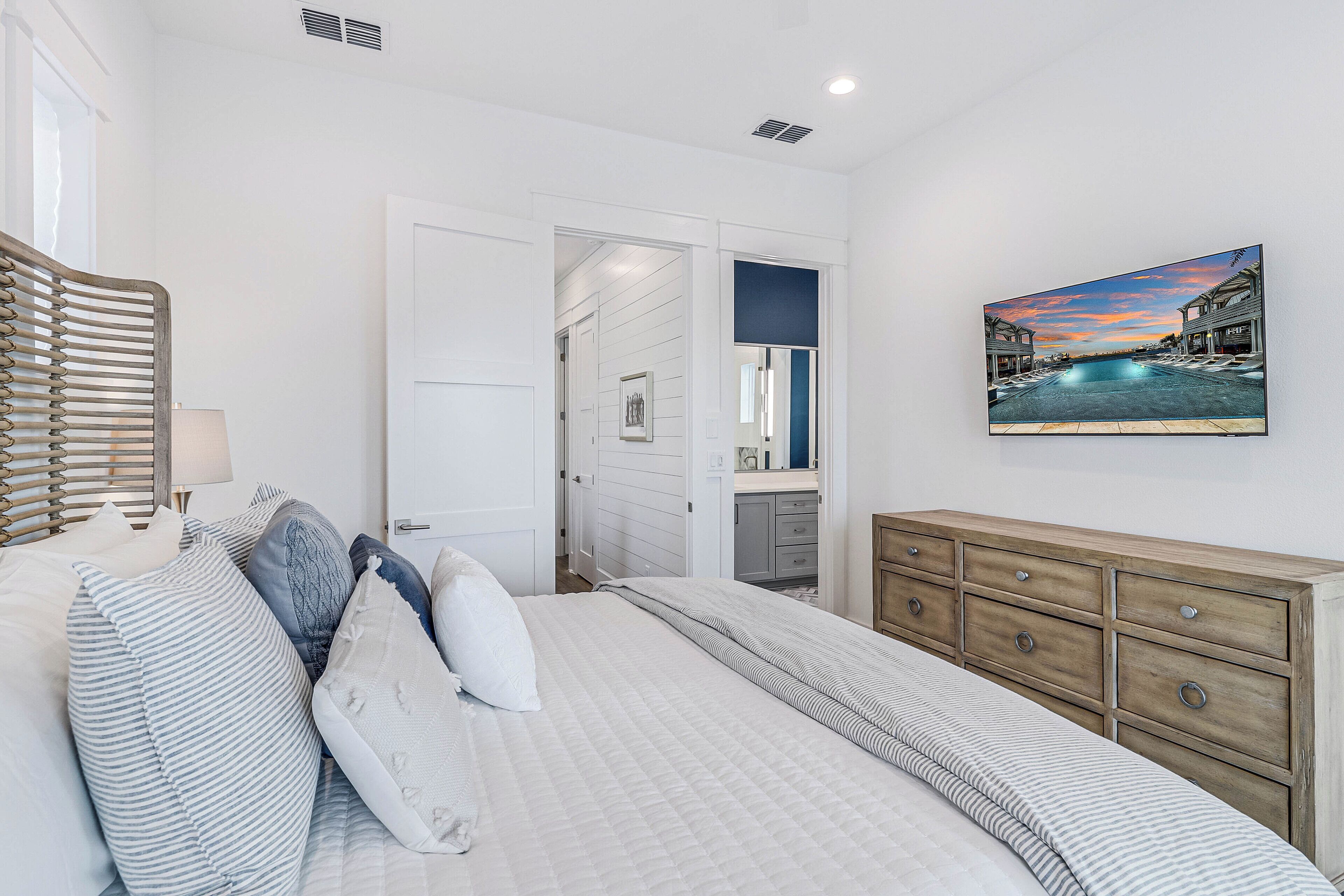 A bedroom with a bed, a dresser, a painting, and a door leading to another room.