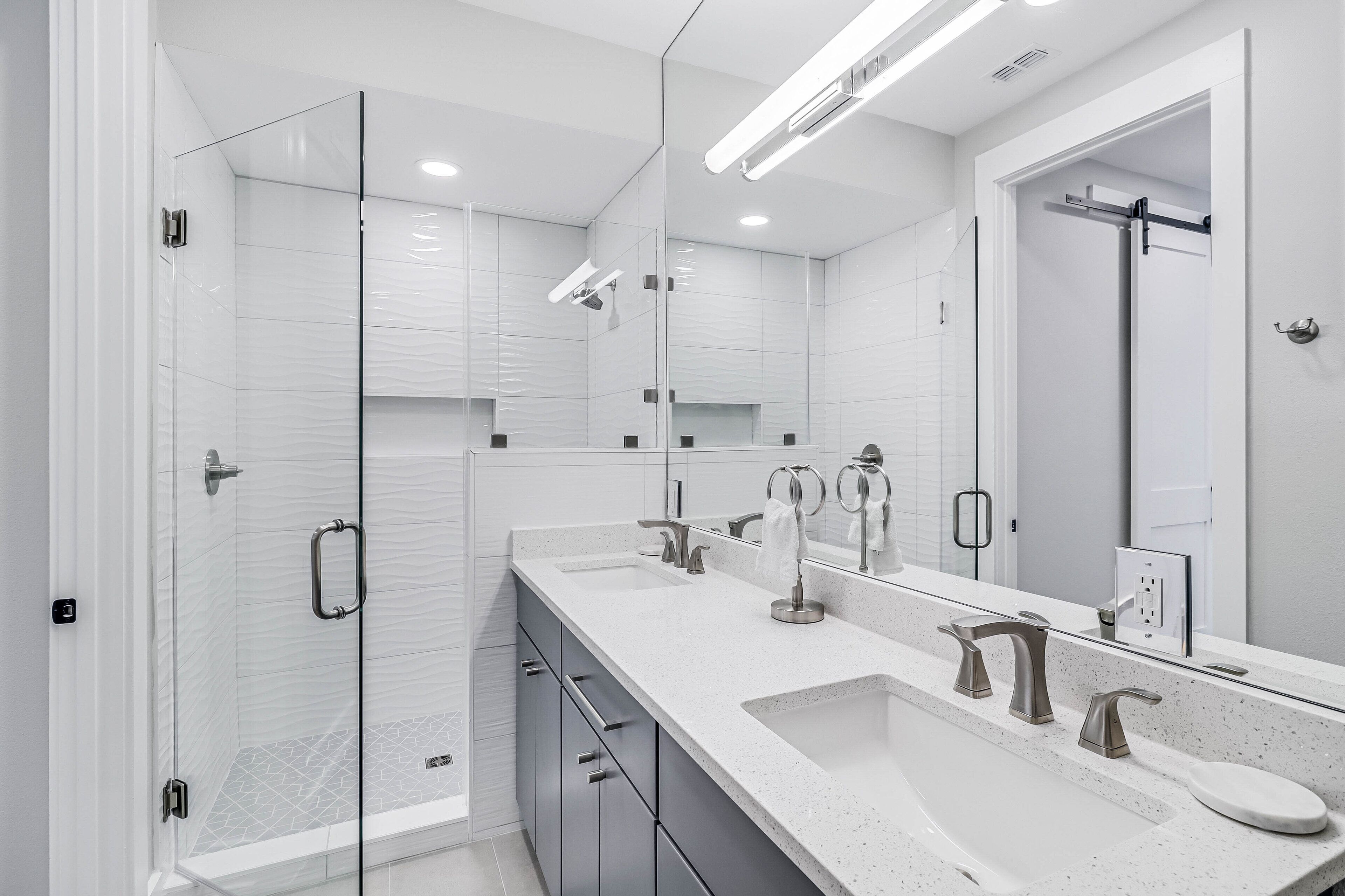 Un baño moderno con cabina de ducha de vidrio, tocador doble y un espejo grande.