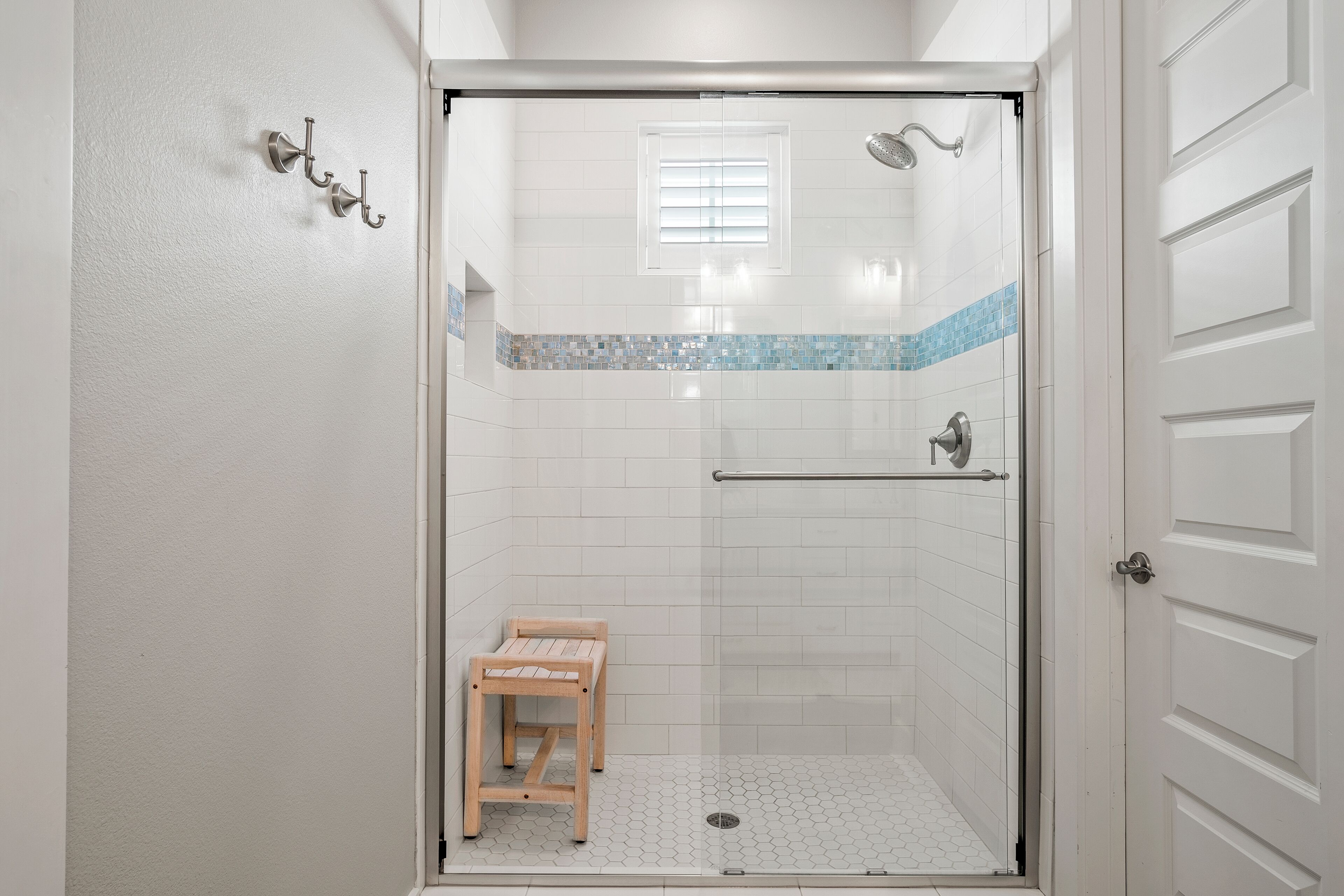 A walk-in shower with a glass door, a wooden bench, and a small window.