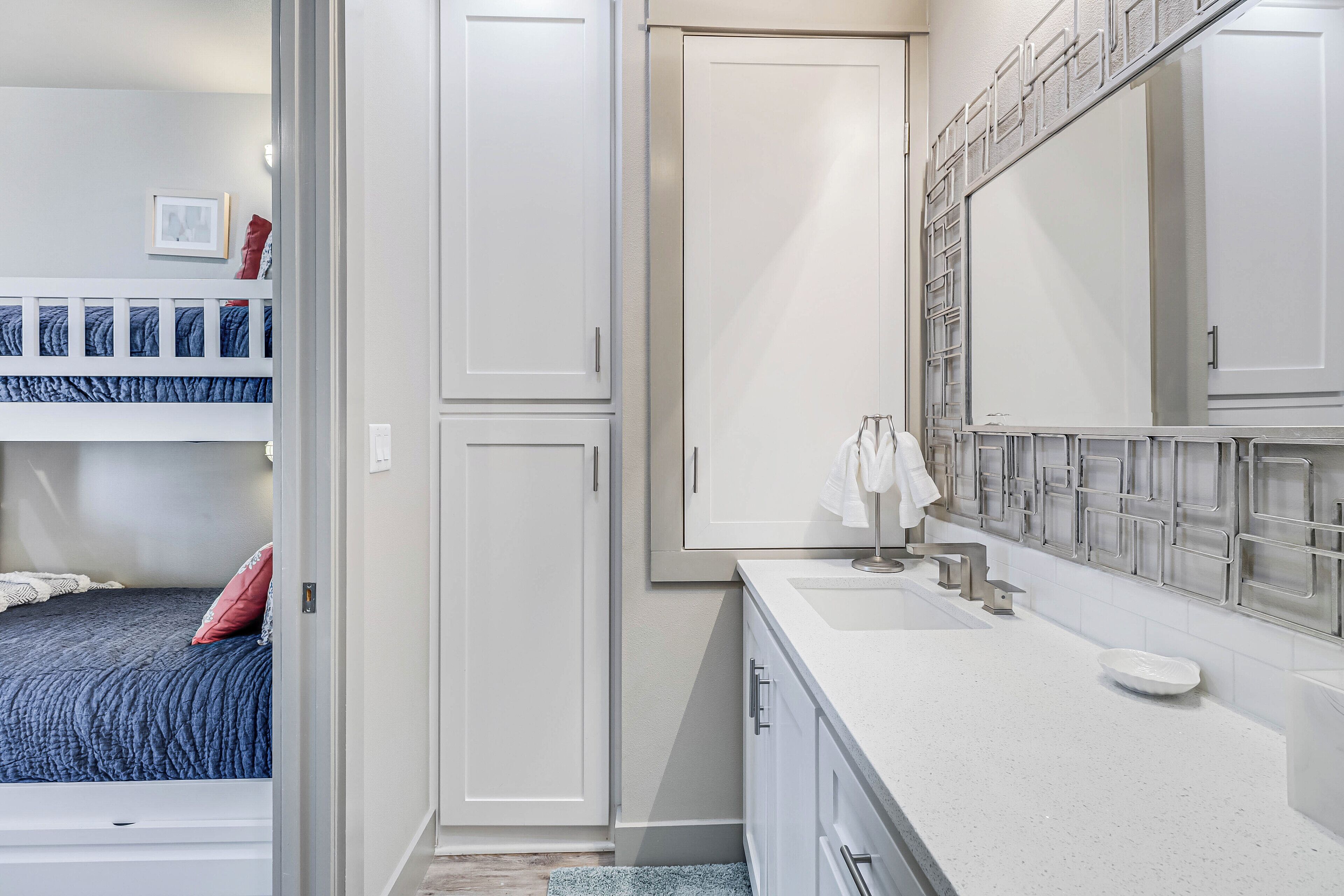 A bedroom with bunk beds, a white wardrobe, a bathroom with a sink and mirror, and a tiled shower area.