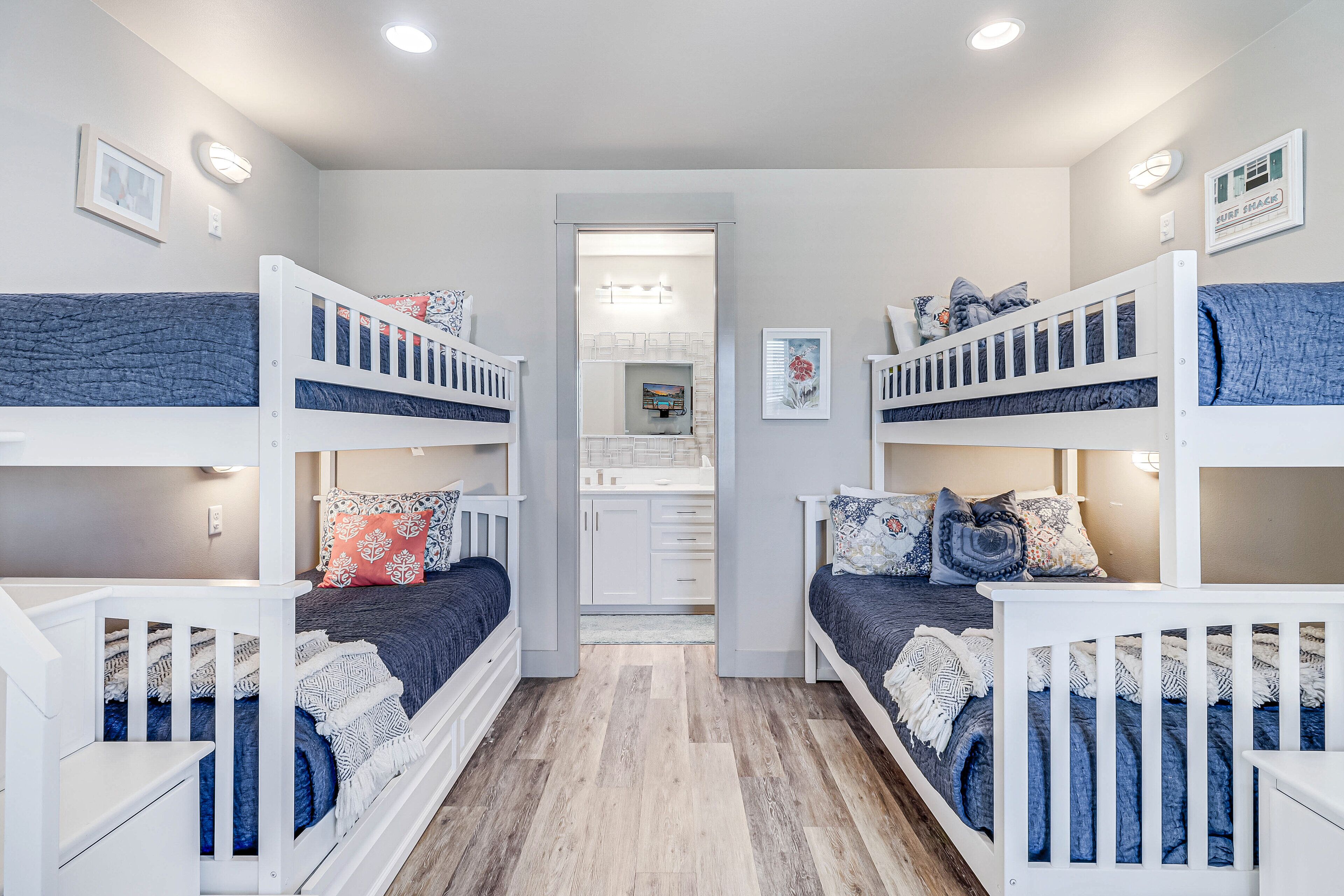 A room with bunk beds, a bathroom with a mirror, and a hallway leading to a kitchen.