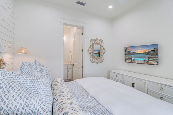 A bedroom with a bed, a nightstand, a dresser, a mirror, and a painting on the wall. - Tarpon Tango TC 8103 (Port Aransas)