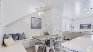 Une cuisine moderne avec une table à manger en bois, des chaises blanches et un luminaire suspendu.