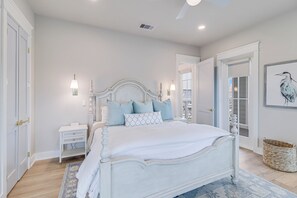 A bedroom with a white bed, light blue bedding, and a nightstand with a lamp. - Easy Breezy 225 TEA (Port Aransas)