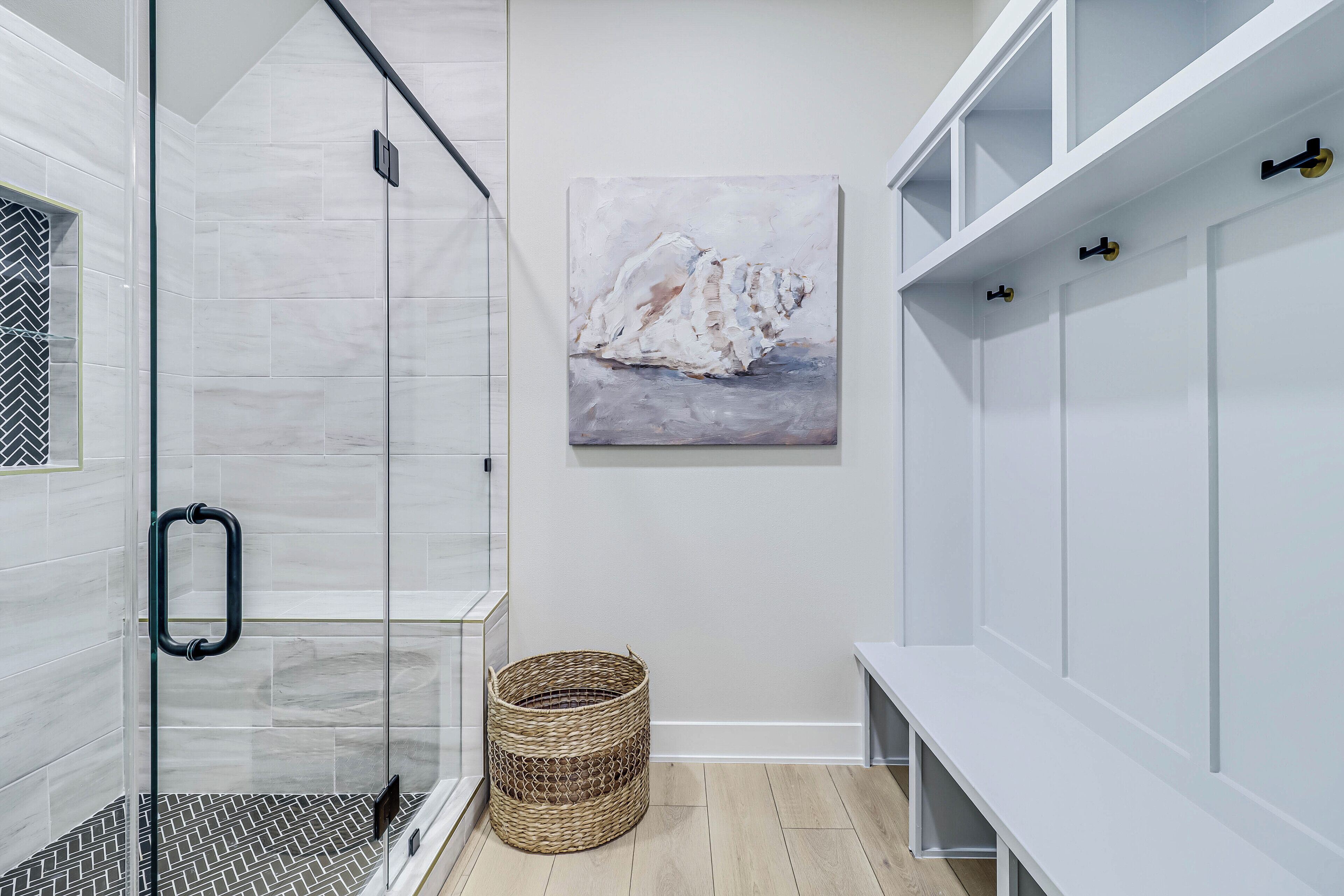 Een moderne badkamer met een glazen douche, een houten vloer, een witte bank en een schilderij van een zeilboot.