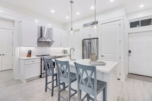 A modern kitchen with white cabinetry, a stainless steel refrigerator, and a central island with bar stools. - Beach Daze TC 8101 (Port Aransas)