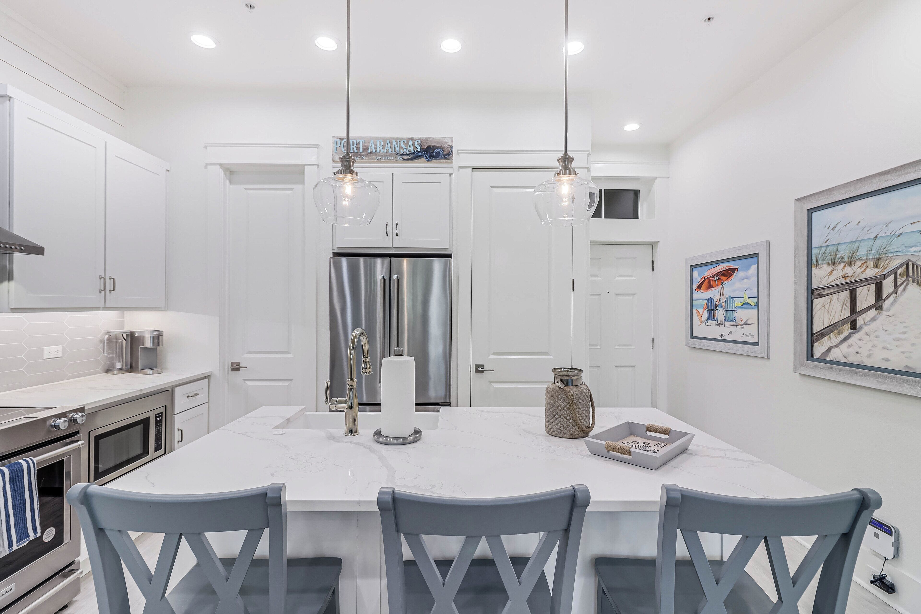 Una cocina moderna con armarios blancos, electrodomésticos de acero inoxidable e iluminación colgante.