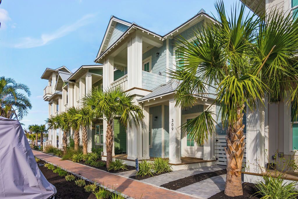 Une rangée de maisons de style côtier, dotées de balcons, de palmiers et d’une promenade pavée.