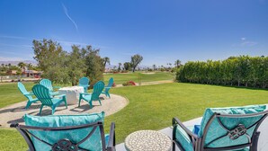 Eine Terrasse mit Gartenmöbeln, einem runden Tisch und Blick auf einen Golfplatz.