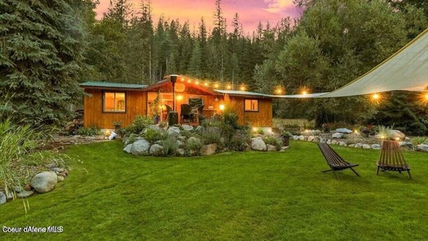 A wooden cabin with a porch, surrounded by a well-maintained lawn and a forest backdrop. - Priest Lake - Escape to the Lake (Nordman)