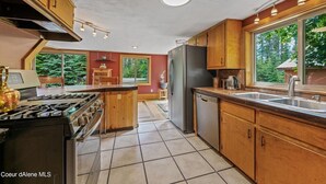 A modern kitchen with wooden cabinets, a central island, a refrigerator, and a dishwasher. - Priest Lake - Escape to the Lake (Nordman)
