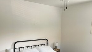 A neatly made bed with a white quilt, two bedside tables with lamps, and a ceiling fan. - Hill Cottage (Park River)